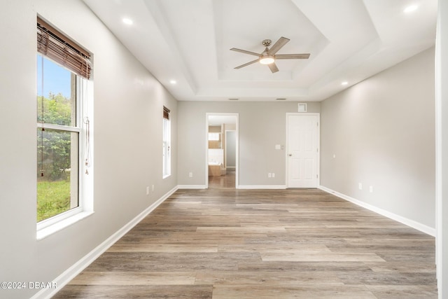 empty room with light hardwood / wood-style floors, ceiling fan, a healthy amount of sunlight, and a tray ceiling