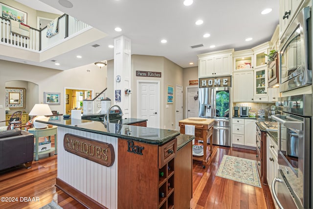 kitchen with stainless steel appliances, dark hardwood / wood-style floors, a center island, and dark stone countertops