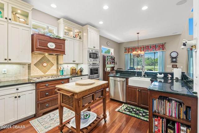 kitchen with appliances with stainless steel finishes, dark hardwood / wood-style floors, pendant lighting, sink, and a chandelier