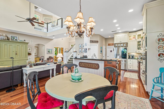 dining room with a high ceiling, sink, ceiling fan with notable chandelier, and light hardwood / wood-style flooring