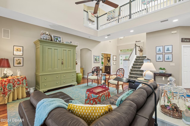 living room featuring ceiling fan, a towering ceiling, and wood-type flooring