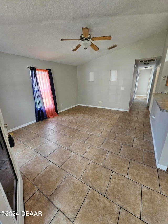 empty room featuring tile patterned flooring, a textured ceiling, ceiling fan, and vaulted ceiling