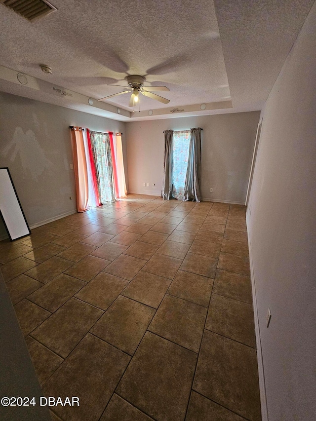 spare room with a textured ceiling, tile patterned flooring, ceiling fan, and a tray ceiling