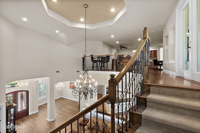 staircase featuring wood-type flooring, a raised ceiling, and ceiling fan with notable chandelier