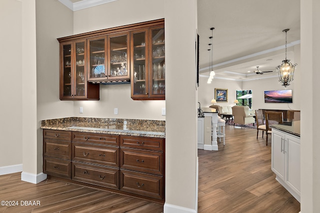 bar with ornamental molding, dark brown cabinetry, dark hardwood / wood-style flooring, light stone countertops, and ceiling fan