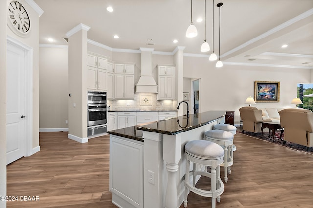 kitchen featuring white cabinets, light wood-type flooring, a kitchen island with sink, and premium range hood