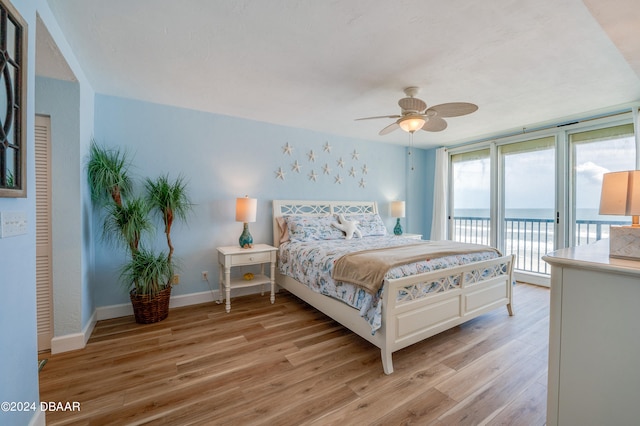 bedroom with ceiling fan, access to exterior, a water view, and light hardwood / wood-style flooring