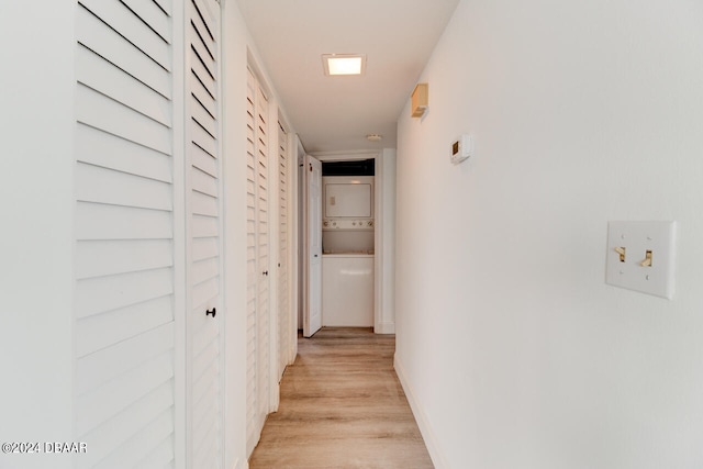 corridor with stacked washer and clothes dryer and light hardwood / wood-style flooring