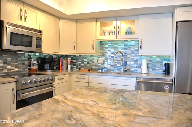 kitchen with light stone counters, appliances with stainless steel finishes, decorative backsplash, sink, and white cabinets