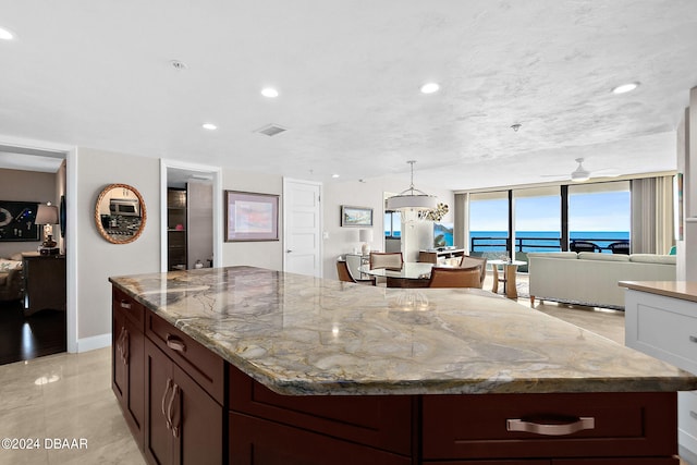 kitchen featuring dark brown cabinetry, a water view, light stone countertops, ceiling fan, and pendant lighting