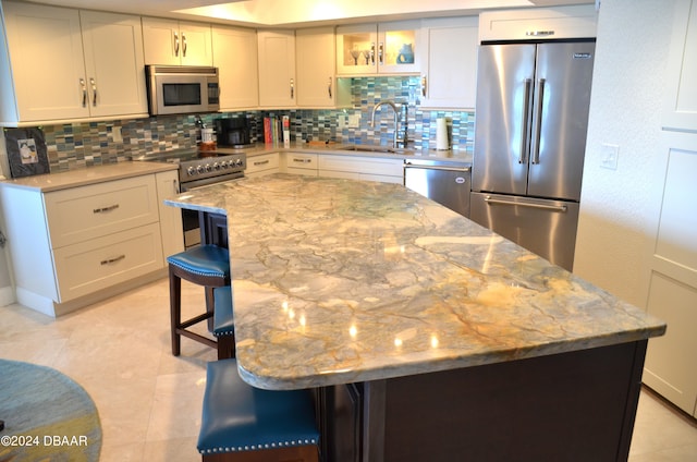 kitchen with sink, light stone counters, appliances with stainless steel finishes, a kitchen bar, and a center island