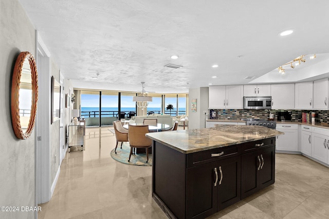 kitchen with white cabinetry, a water view, light stone counters, backsplash, and a center island