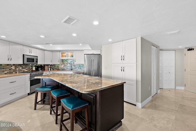 kitchen featuring a kitchen breakfast bar, high quality appliances, a kitchen island, light stone countertops, and white cabinetry