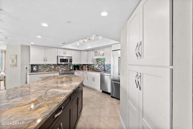 kitchen with tasteful backsplash, light stone counters, white cabinetry, appliances with stainless steel finishes, and sink