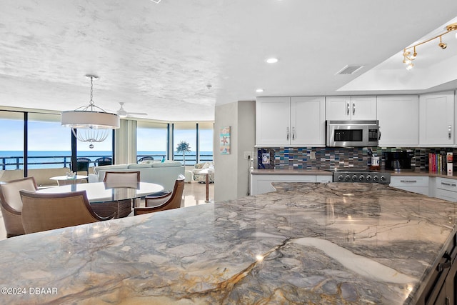 kitchen featuring a water view, decorative backsplash, hanging light fixtures, stone countertops, and white cabinetry