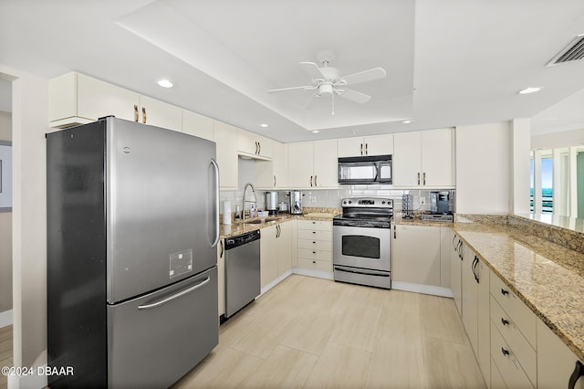 kitchen with sink, appliances with stainless steel finishes, light stone countertops, backsplash, and a raised ceiling