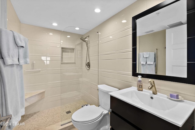 bathroom featuring toilet, vanity, a tile shower, and tile walls