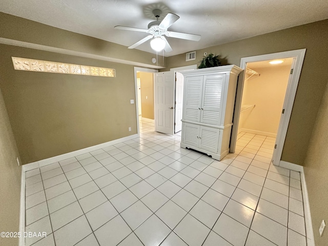 unfurnished bedroom with light tile patterned flooring, baseboards, a ceiling fan, and a spacious closet