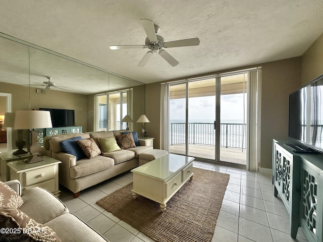 living room with a ceiling fan, healthy amount of natural light, light tile patterned floors, and a textured ceiling