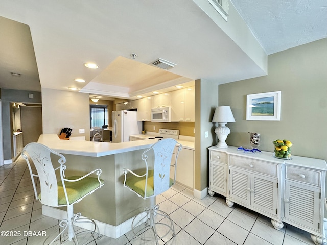 kitchen featuring white appliances, a kitchen breakfast bar, light countertops, a peninsula, and light tile patterned flooring
