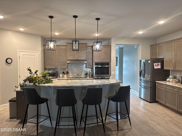 kitchen featuring pendant lighting, stainless steel appliances, a center island with sink, and light hardwood / wood-style flooring