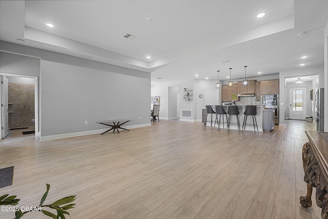 living area featuring a tray ceiling, recessed lighting, visible vents, light wood-style flooring, and baseboards