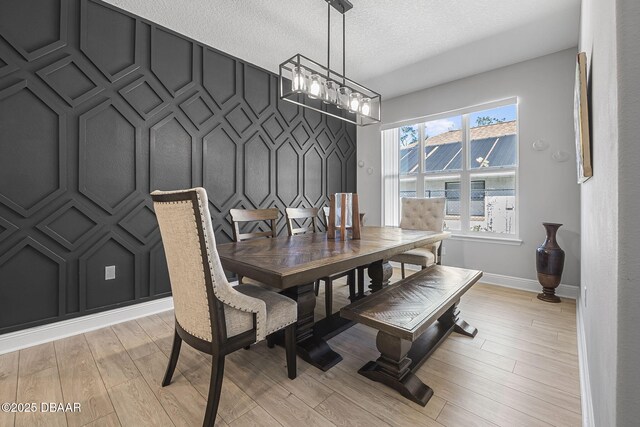 dining room with a decorative wall, light wood-style flooring, an inviting chandelier, an accent wall, and a textured ceiling