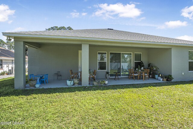 back of property with roof with shingles, a lawn, a patio area, and stucco siding