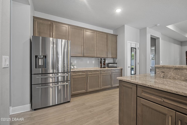 kitchen with a textured ceiling, light wood finished floors, light stone countertops, and stainless steel fridge with ice dispenser