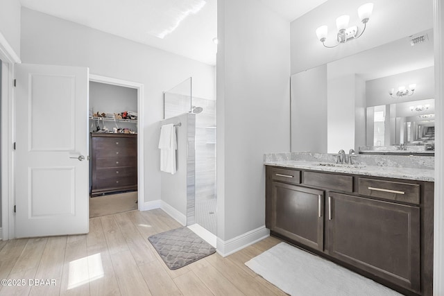 bathroom featuring visible vents, wood finished floors, a spacious closet, vanity, and a walk in shower