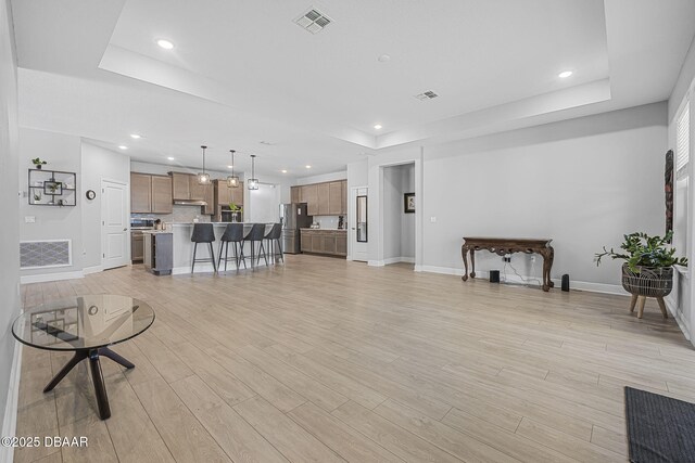 living room featuring light wood-type flooring, a raised ceiling, visible vents, and recessed lighting