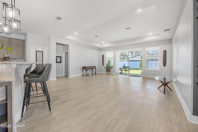 living room featuring a tray ceiling, visible vents, and light wood finished floors