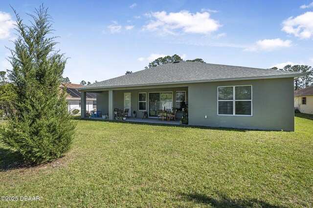 rear view of property with a shingled roof, a lawn, a patio area, and stucco siding