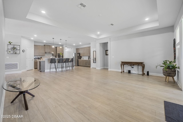 living room featuring light wood-type flooring, a tray ceiling, visible vents, and recessed lighting