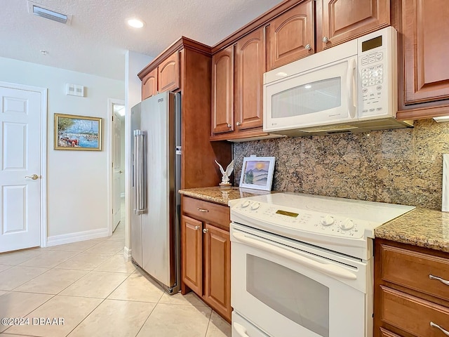 kitchen with white appliances, light tile patterned floors, visible vents, brown cabinets, and backsplash