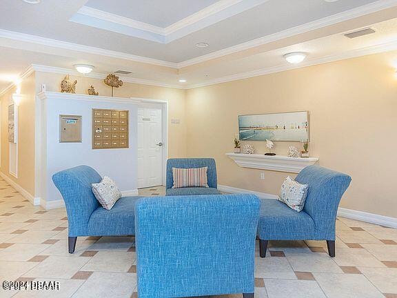 living area with baseboards, visible vents, a raised ceiling, mail area, and crown molding