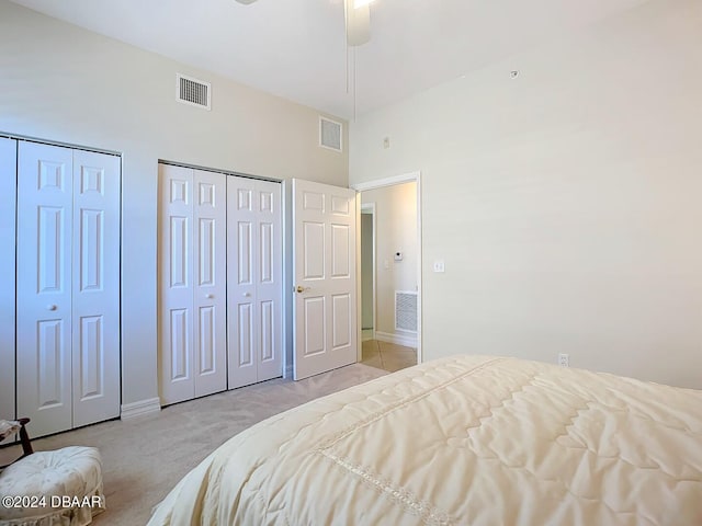 bedroom featuring ceiling fan, a high ceiling, light colored carpet, and multiple closets