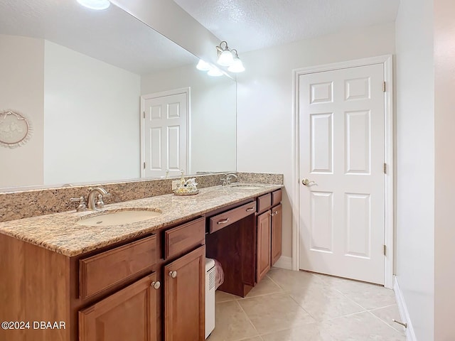 bathroom with double vanity, a textured ceiling, a sink, and tile patterned floors