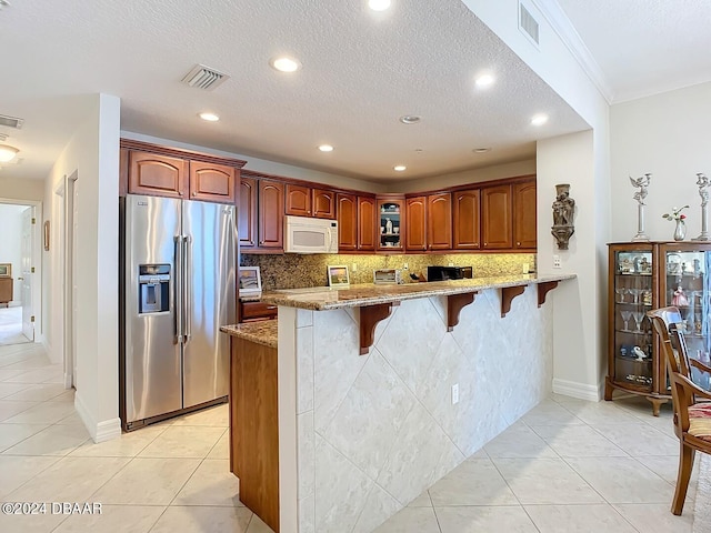 kitchen featuring white microwave, light stone counters, a peninsula, stainless steel fridge with ice dispenser, and a kitchen bar