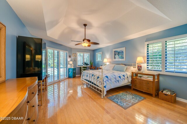 bedroom with access to exterior, a tray ceiling, light hardwood / wood-style floors, and ceiling fan