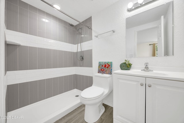 bathroom featuring toilet, a tile shower, wood finished floors, vanity, and a textured wall