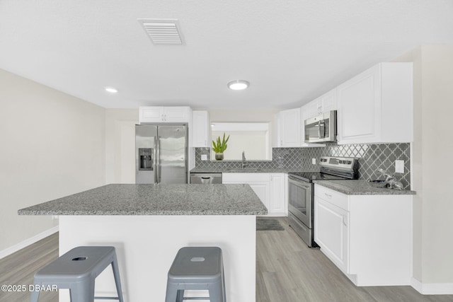 kitchen featuring stainless steel appliances, a sink, a breakfast bar, light wood finished floors, and white cabinets