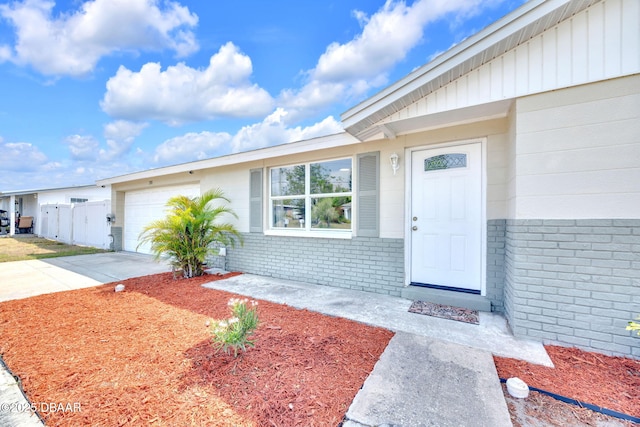 view of exterior entry with a garage, driveway, brick siding, and fence