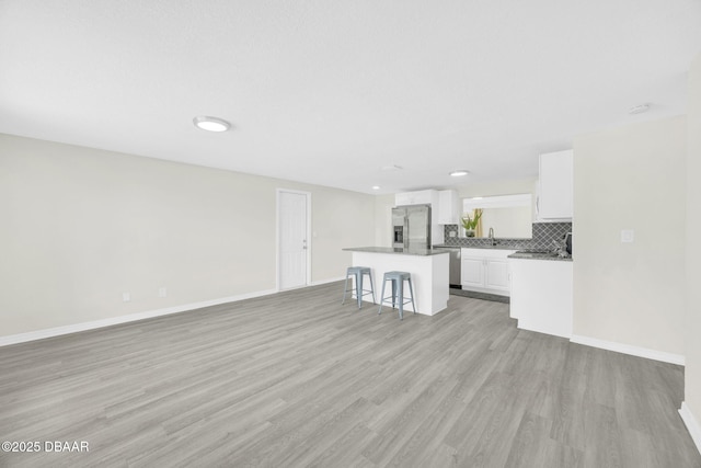 unfurnished living room featuring light wood finished floors, baseboards, a sink, and recessed lighting