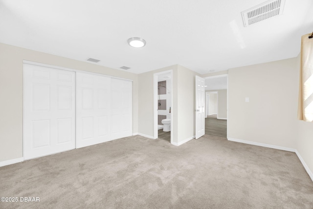 unfurnished bedroom featuring carpet floors, baseboards, a closet, and ensuite bath