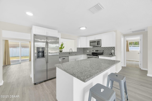 kitchen featuring stainless steel appliances, a sink, a center island, backsplash, and baseboards
