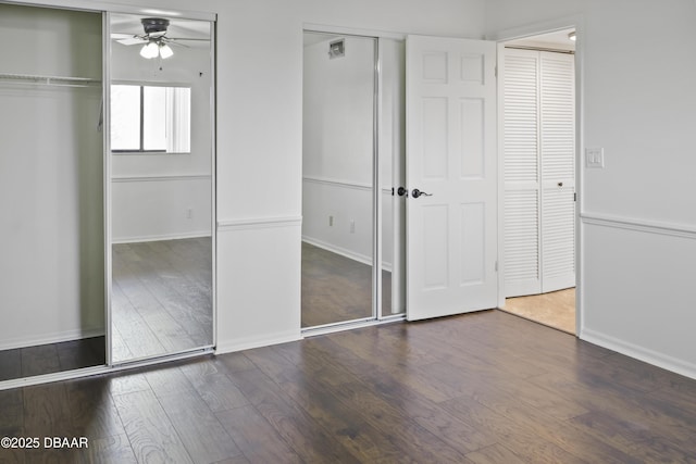 unfurnished bedroom featuring baseboards, dark wood-type flooring, and multiple closets