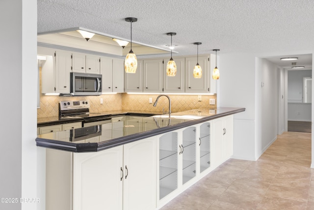 kitchen featuring decorative light fixtures, dark countertops, appliances with stainless steel finishes, white cabinetry, and a peninsula