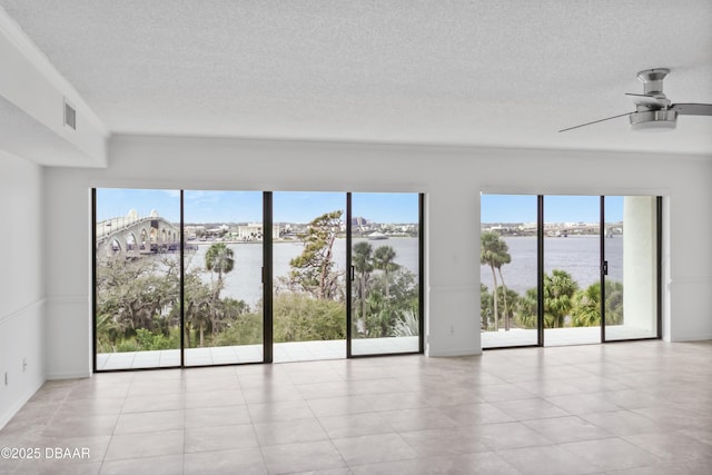 unfurnished room with a ceiling fan, a water view, visible vents, and a textured ceiling