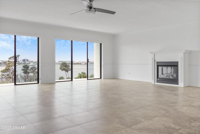 unfurnished living room with a water view, a glass covered fireplace, a wealth of natural light, and a ceiling fan